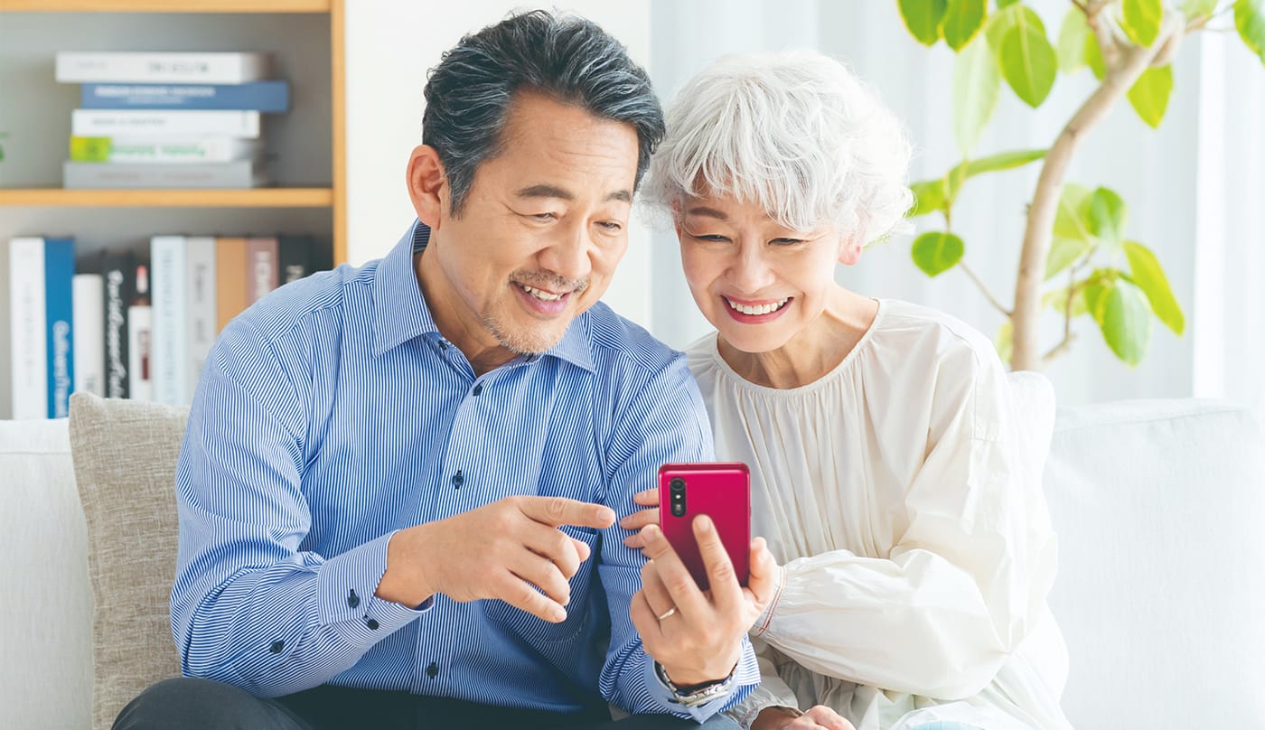 高齢の男女が簡単に操作できるスマートフォンのホーム画面を一緒に見ている様子